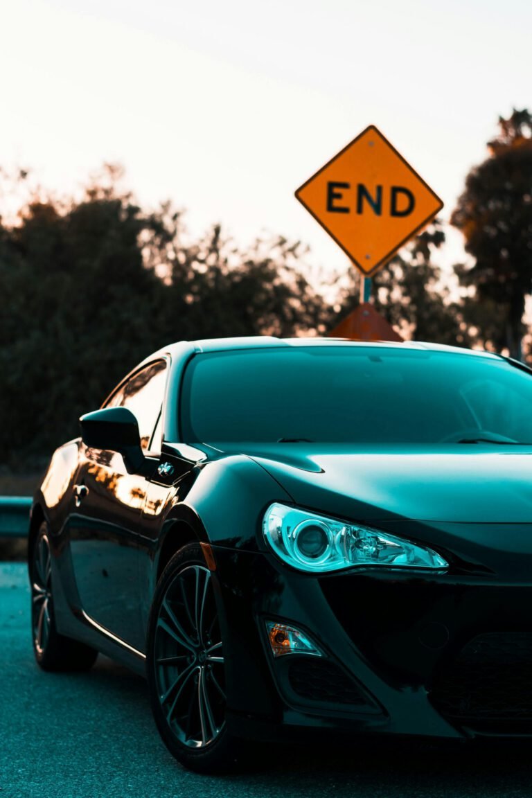 A car parked with a setting sun, in front of a yellow diamond square street sign that reads "END".