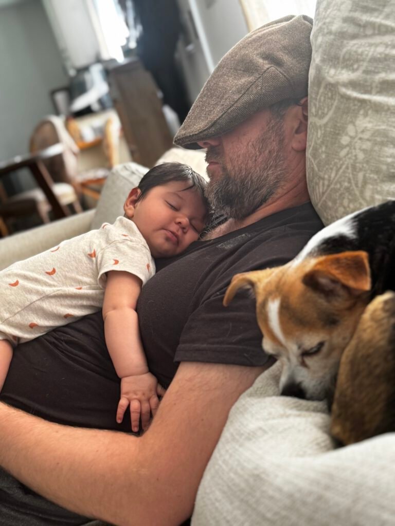 A father, infant son, and small dog sleeping peacefully together on a couch.
