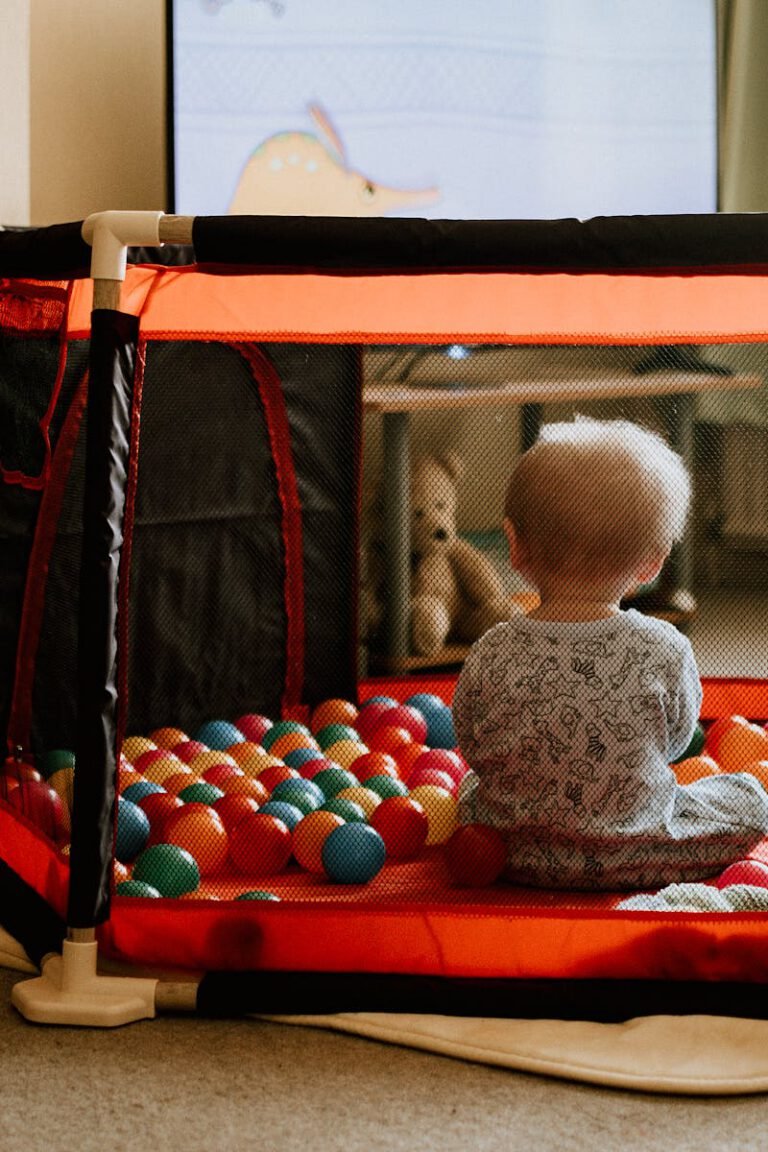 Toddler sitting in play pen filled with ball pit balls and watching television.